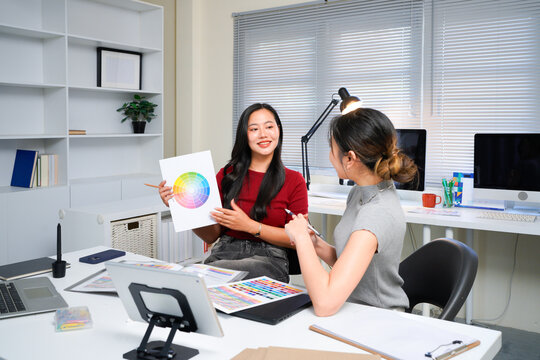 Two professional women collaborating on creative design project, discussing colorful color swatches, hues, and palettes at modern office workspace table. Ideal for wallpaper, poster - Powered by Adobe