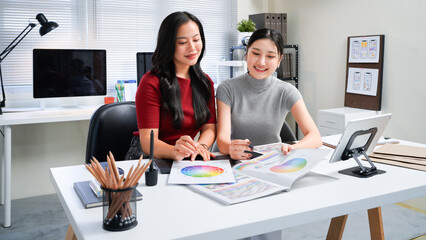 Fototapeta premium Two professional women collaborating on creative design project, discussing colorful color swatches, hues, and palettes at modern office workspace table. Ideal for wallpaper, poster