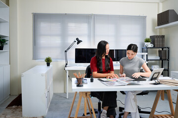 Two professional women collaborating on creative design project, discussing colorful color swatches, hues, and palettes at modern office workspace table. Ideal for wallpaper, poster