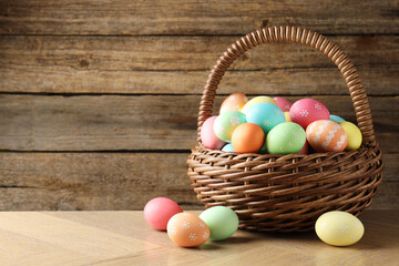 Beautiful decorated Easter eggs in wicker basket on wooden table, space for text