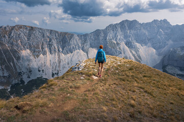 Fototapeta premium Hiker walks narrow path to sunlit hilltop view rocky mountain ridge on sunny day, Durmitor, Montenegro