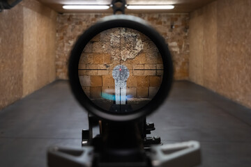 First person view through a rifle scope aiming at a metal gong target in an indoor professional shooting range gallery.