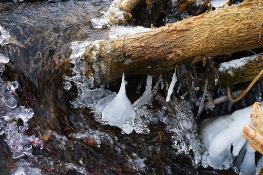 A stream flows between blocks of ice in a winter landscape. The ice forms intricate, natural patterns.