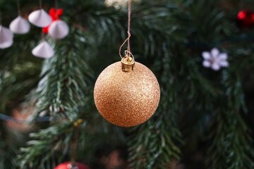 Eine goldene Kugel, mit Glitzer bedeckt, glänzt an den Zweigen des Weihnachtsbaums und reflektiert...