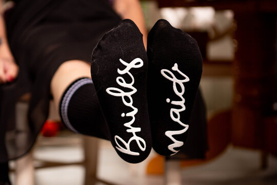 Close-up of black socks worn by a bridesmaid with the word "Bride" written on one sole and "Maid" on the other in cursive lettering. Fun and creative wedding day detail for bridal party content