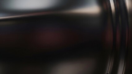 Reflective metallic surface with blurred highlights and dark, smooth texture, abstract background.