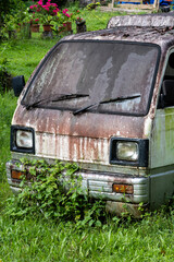 Abandoned rusty utility vehicle overgrown with vegetation &mdash; weathered truck in tropical garden setting, evoking nostalgia and decay, characteristic of rural Philippines (Bohol, Panglao)