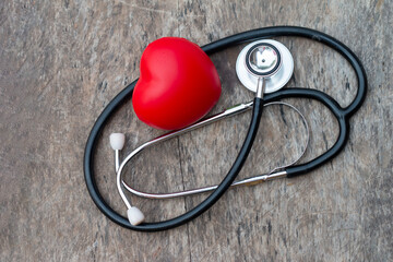 Medical stethoscope with red heart symbol placed on weathered wooden floor.