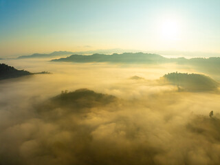 Fototapeta premium Aerial view of flowing fog waves on mountain tropical rainforest,Bird eye view image over the clouds Amazing nature background with clouds and mountain peaks in Thailand