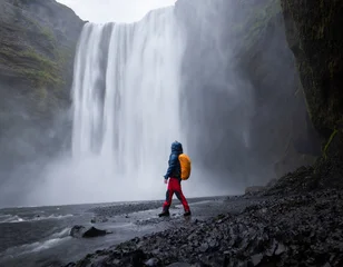 Gardinen Grau Hiker getting wet as enjoying views on big beautiful waterfall in front of him, Iceland  © Peter Kolejak