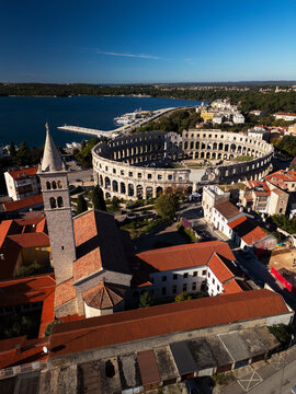 Pula Arena ancient Roman amphitheater with historic city skyline and orange roofs aerial drone view.
