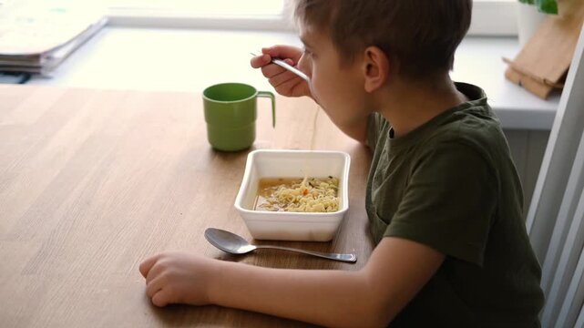 6 years old boy eats instant noodle from box. Child is eating spaghetti. Lunch time. A good appetite. Tasty children food. Close-up portrait. Carbs dinner. Fast food. Kid eating by himself with fork.