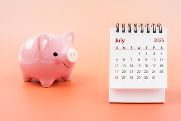 Desk calendar for July 2026 and pink piggy bank.