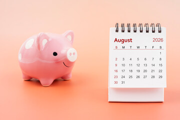 Desk calendar for August 2026 and pink piggy bank.