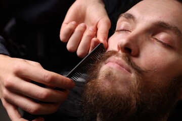 Barber styling man's mustache in barbershop, closeup