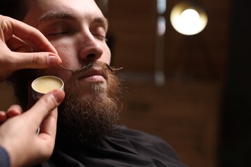 Barber styling man's mustache with wax in barbershop, closeup. Space for text