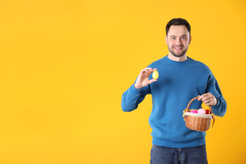 Naklejka premium Easter celebration. Smiling man with wicker basket full of painted eggs on yellow background, space for text