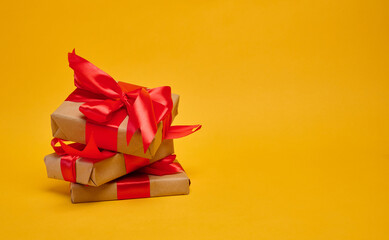 Gifts wrapped in brown paper and red satin ribbon on a yellow background
