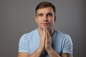 Young man praying on light grey background