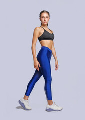 Young fitness athletic woman wearing blue legging and black top posing touching her leg looking at camera with determination discipline expression stand on white background