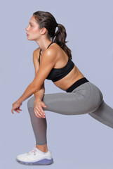 Stretching Young fitness athletic woman wearing grey legging and black top posing looking at camera with determination discipline expression on white background