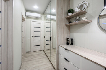  A narrow modern hallway with light wood flooring, white doors with black inserts, built-in...