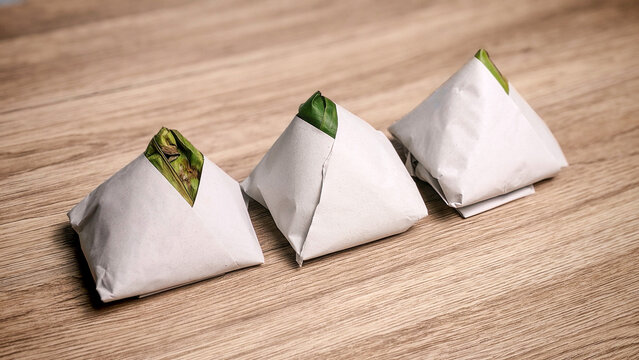 Traditional packs of nasi lemak wrapped in banana leaf and paper on wooden table background