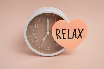 Alarm clock with relax text on heart sticker against peach background. Time for relaxation concept. 