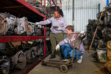 Workers working in a auto parts warehouse, examining salvaged parts. The warehouse is...