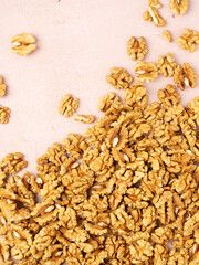 top view of shelled walnut halves scattered across a light pink textured background. The composition is minimalistic, with most walnuts gathered in the lower part of the frame, creating a natural, org