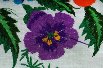 Naklejka premium Hand embroidered purple pansy flower on white linen fabric