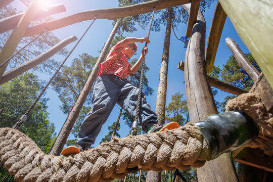 Agile boy quickly climb rope on playground structure in forest