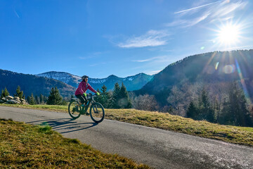 Fototapeta premium Active senior woman rides an electric mountain bike on a forest trail in the Allgäu Alps near Steibis-Oberstaufen at sunset, enjoying autumn scenery and outdoor activity.