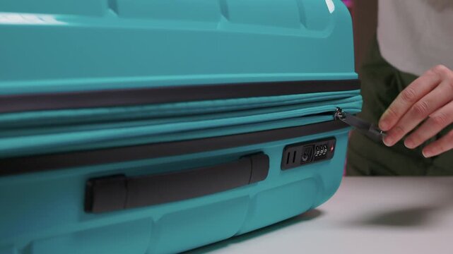 Traveler opening luggage, Close shot of hands unfastening suitcase zipper before travel, Detailed view of hands pulling zipper on vibrant teal travel case with anticipation