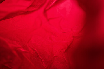 Extreme close up of red empty plastic bag background. The plastic surface is wrinkly and tattered making abstract pattern. Selective focus, shallow depth of field.
