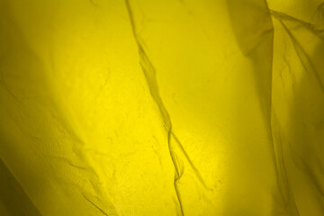 Extreme close up of yellow empty plastic bag background. The plastic surface is wrinkly and tattered making abstract pattern. Selective focus, shallow depth of field.