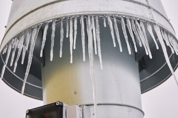 Metal vent with hanging icicles, Frozen icicles draping metallic chimney vent, Closeup of icy metal...