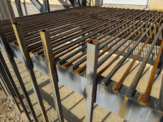 Rusty steel grating exhibits significant wear and tear in an outdoor setting. Sunlight highlights the corroded bars and supports, creating a rustic industrial atmosphere.