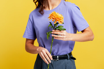 Woman holding vibrant orange dahlia flower against bright yellow background