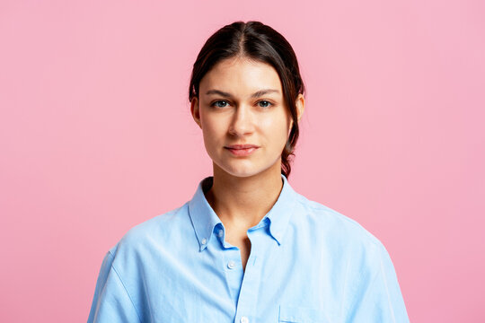 Young woman posing casually with neutral expression against pink background