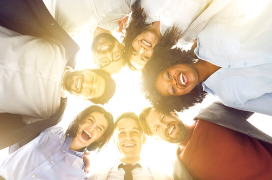 Group portrait taken from below of smiling multinational team of an office workers, standing in circle and looking at the camera together. Teamwork and business unity in the office environment.