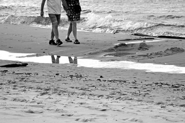 ludzie spacerujący po piaszczystej plaży, odbicie w wodzie, czarno-białe, people walking on the sandy beach, legs reflected in the water