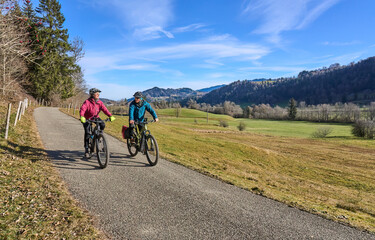 Naklejka premium elderly couple rides electric mountain bikes on a trail in the Allgäu Alps near Oberstaufen in Bavaria. The scene depicts a wintry mountain landscape in early winter.