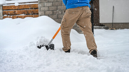 Clearing snow from a driveway using a winter shovel. Winter sidewalks maintenance.
