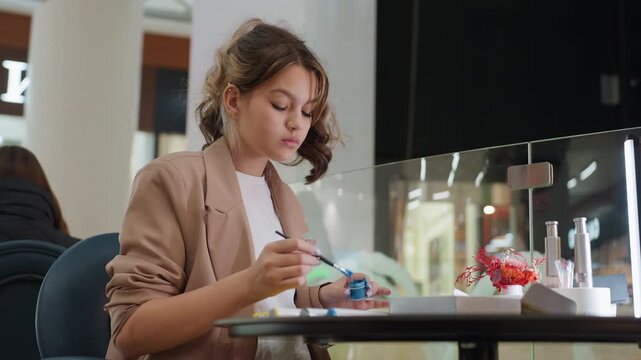 woman crafting intricate nail art by hand, young woman carefully designing tiny patterns on her nails, young woman expertly uses precision instrument to decorate her nails with delicate patterns