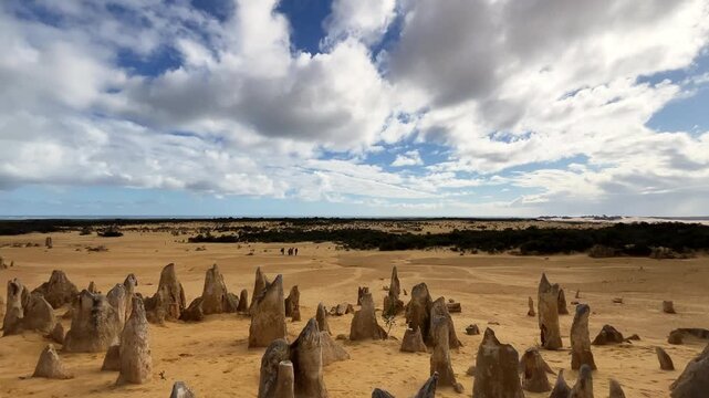 Visitors explore the Pinnacles Desert where tall rock formations rise from the sand beneath a cloudy sky in Western Australia