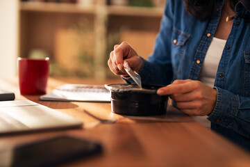 Woman opening takeout food container at desk during lunch break