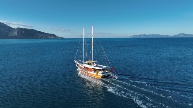 Sailing into Adventure: A sleek sailboat cuts through the turquoise waters, its sails billowing gently in the breeze. The vessel appears to be traveling near the mountains