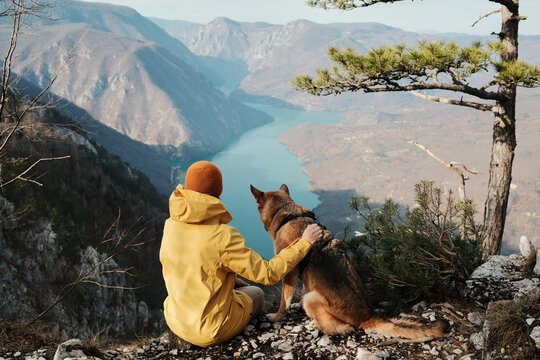 A woman gently hugs a German Shepherd on viewpoint above the Drina river canyon in Tara National park, Serbia. Concept of trust companionship and outdoor adventure with dogs.