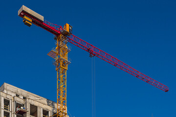 Under construction multi-storey building with tower type construction crane on clear blue sky background with perspective. Housing industry, real estate investment at stage of construction of walls